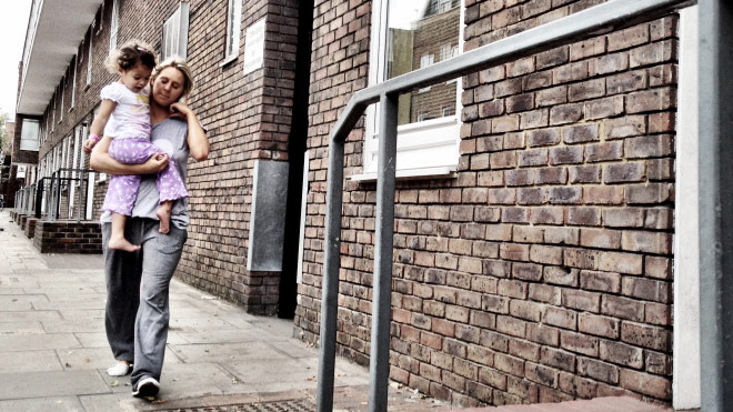 A mother walks down the street with a baby in her arms