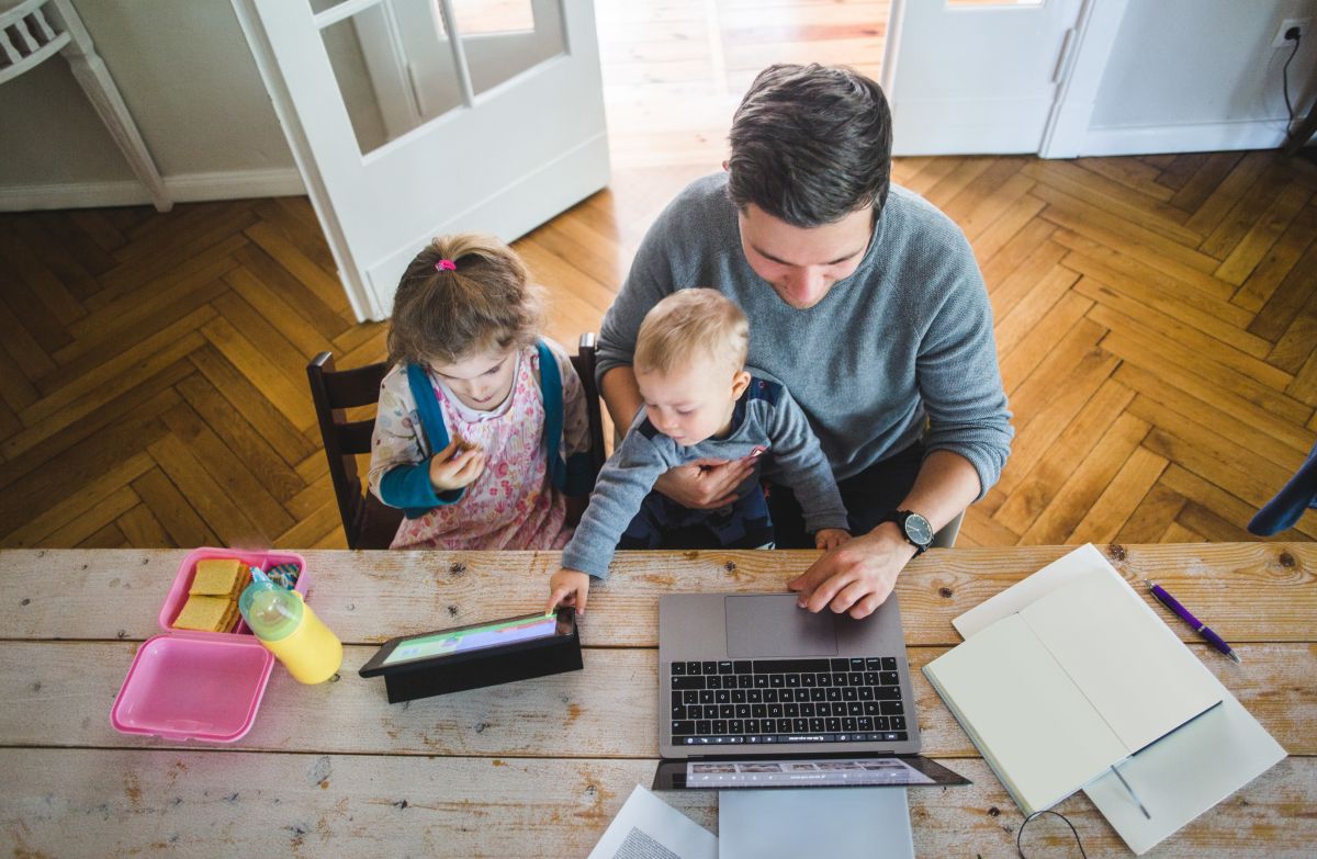 High angle view of man using laptop while sitting with children looking at digital tablet