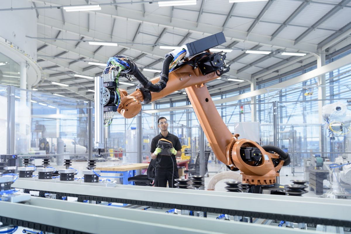 A factory worker holding a control pad manipulates a large robot 