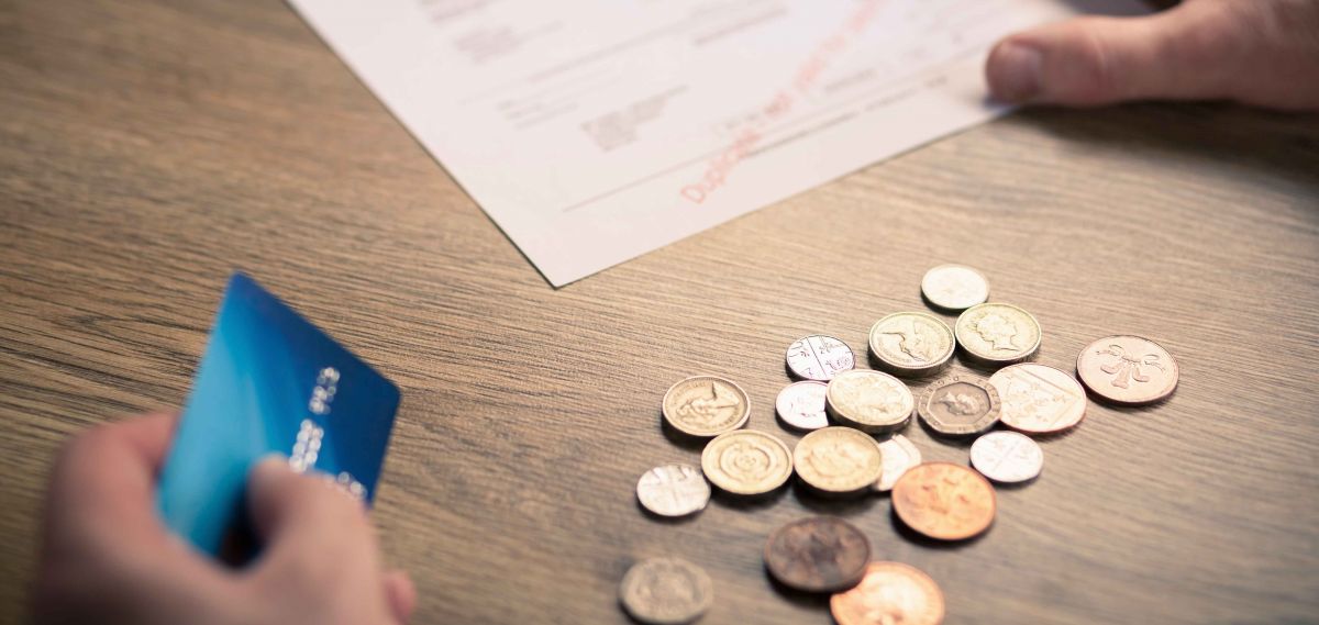 Image of two hands, one holding a credit card, the other a bill and some coins on a table