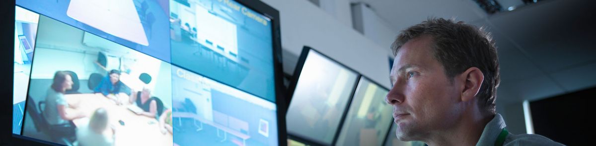 Man looking at screens showing people sitting around a table in an office