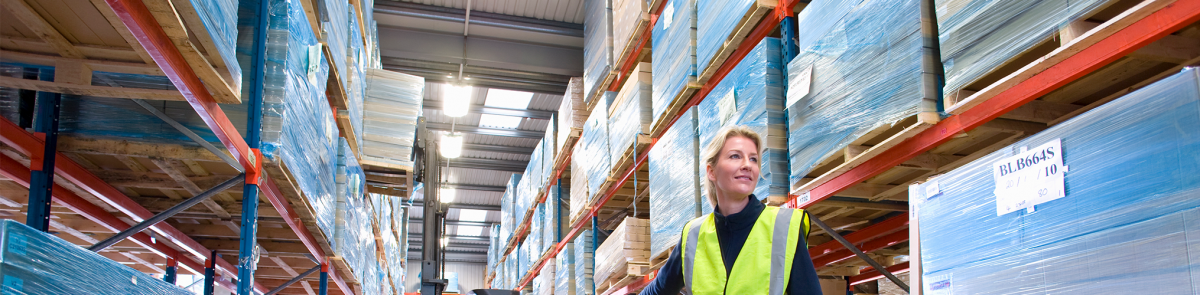 Female warehouse manager holding clipboard and pulling pallet truck