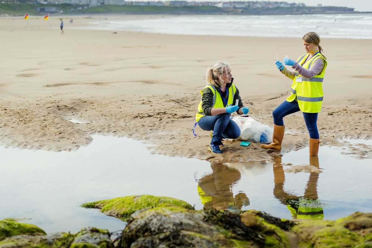 Two women workers taking water samples from a beach to assess environmental damage