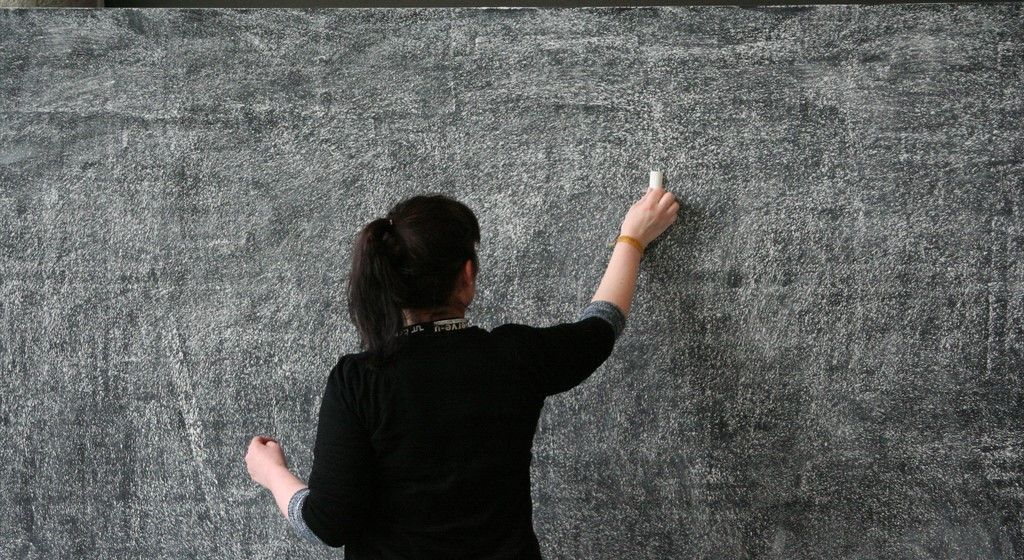 A female teacher writes on a black board