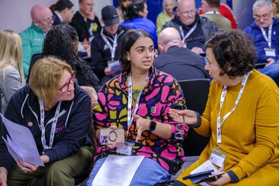 A woman in a yellow top, a woman in a pink and blue fleece and a woman in a navy blue hoodie discussing in a workshop