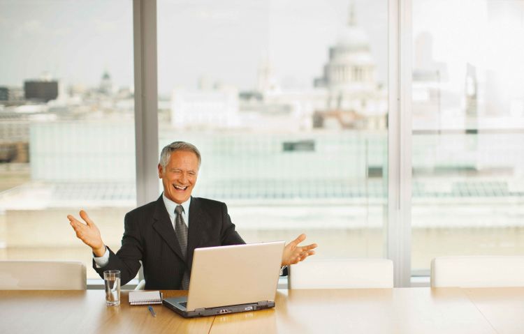 A laughing business man looks at a laptop screen in a boardroom overlooking St Paul's cathedral in London