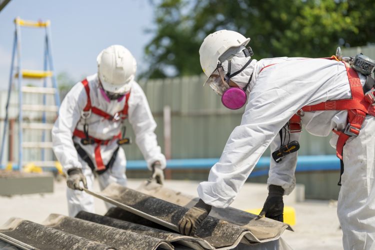 Workers wearing full body protective clothing while working with the asbestos roof tiles