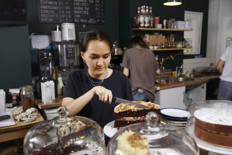 A waitress in a cafe cutting a slice of cake - stock photo