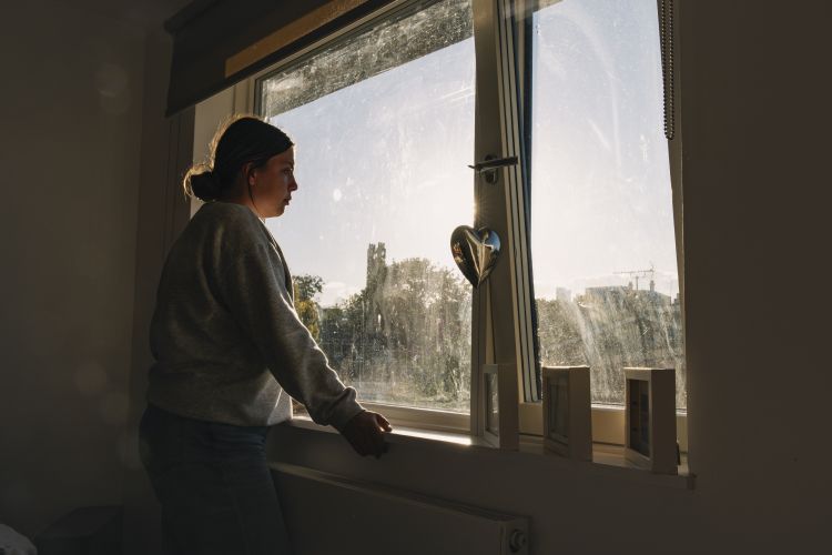 Young woman looks out of her bedroom window - negative emotion