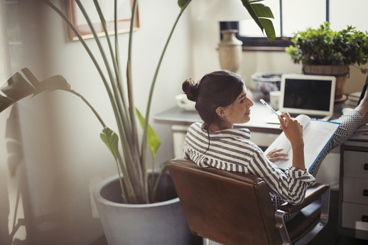 Businesswoman reading paperwork with feet up on desk