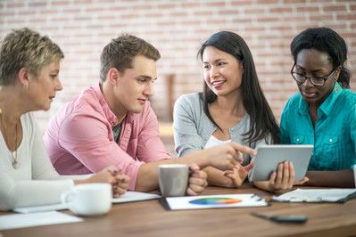 A group of four workers sitting together looking at the same information on a tablet