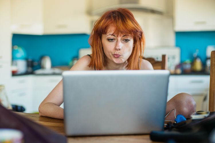 Women looks at her laptop while sitting in a kitchen (c) getty