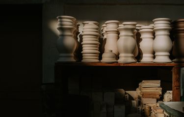 Various shaped, unglazed vases / urns sit in a row, illuminated in sunlight