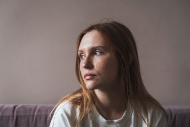Portrait of sad upset redhead girl looking aside thinking about life problems, feeling lonely while spending time alone at home. Mental health, melancholy mood