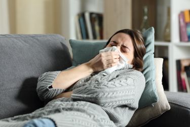 Ill woman blowing nose or coughing using tissue in winter at home