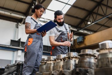 Industrial workers measuring and inspecting mechanical parts in factory - stock photo