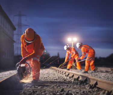 Railway maintenance workers using grinder on track at night