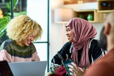 cheerful woman in hijab chatting with female colleague