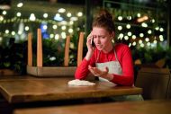 Upset waitress sitting by table and talking to someone by smartphone at the end of working day
