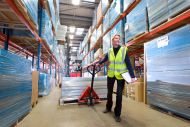 Female warehouse manager holding clipboard and pulling pallet truck