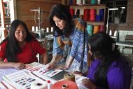 Three women working together, one pointing at a color card on a table of textiles