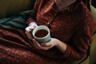 Portrait of a long-haired red-haired woman sitting on the sofa with cup of tea