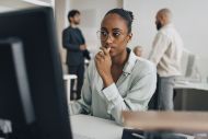 young creative professional wearing eyeglasses sitting at desk while working on desktop PC in office 