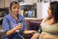 Midwife takes patients blood pressure on home visit