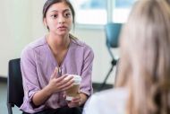 A woman holding a coffee cup in discussion with another woman whose back is to camera