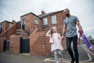 Father and Daughter take a walk along a local street with their scooter.