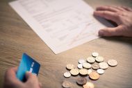 Image of two hands, one holding a credit card, the other a bill and some coins on a table
