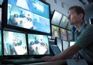 Man looking at screens showing people sitting around a table in an office