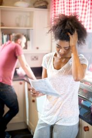 Stressed woman looking at bills with male partner in the background