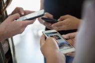 a group of people huddled together staring at their mobile phone screens