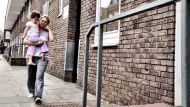 A mother walks down the street with a baby in hand