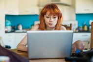 Women looks at her laptop while sitting in a kitchen (c) getty