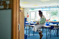Mid adult female teacher sitting on desk with classroom door open 